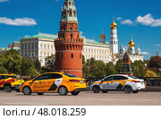 Russia, Moscow, April 28, 2025. Taxi business. A yellow taxi car in motion against the background of the Kremlin in the center of the capital. A trip to the famous sights of Moscow. Редакционное фото, фотограф Photojuli / Фотобанк Лори