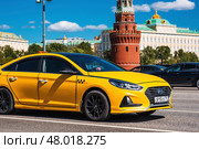 Russia, Moscow, April 28, 2025. Taxi business. A yellow taxi car in motion against the background of the Kremlin in the center of the capital. A trip to the famous sights of Moscow. Редакционное фото, фотограф Photojuli / Фотобанк Лори