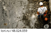 A construction worker digs and levels the soil at an urban construction site under bright sunlight. Стоковое AI-изображение, AI-художник Данила Большаков / Фотобанк Лори