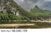 Picturesque mountains on the river bank. Peaks against the sky and clouds. Green vegetation on the slopes. Shallow water and pebbly shoals in the foreground. Reflection. China. Li River. Li Jiang. Стоковое фото, фотограф Вера Ивановна Кубарева / Фотобанк Лори