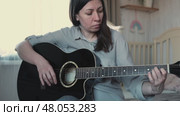 Woman Practicing Guitar in Cozy Room at Home. Strumming black acoustic guitar. Female learning to play music. Person hand on a guitar neck. Guitarist working on melody, performance, practice indoors. Стоковое видео, видеограф Марина Демидюк / Фотобанк Лори