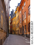 Stockholm.Sweden. Престгатан в Старом городе. Узкая улица Prästgatan в историческом районе Гамла Стан, Стокгольм. Дома окрашены в насыщенные оттенки охры, терракоты и жёлтого, характерные для старой скандинавской архитектуры. Мощёная дорога, закрытые ставни и кованые фонари создают атмосферу старины и уюта. Это одна из самых живописных улиц Старого города. Стоковое фото, фотограф Анна Чижова / Фотобанк Лори