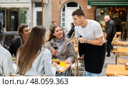 On open area of cafe, guy waiter communicates with couple of customer, accepts order. Стоковое фото, фотограф Яков Филимонов / Фотобанк Лори