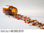 Colorful pills spill from an overturned bottle on a dark surface. Разноцветные таблетки высыпаются из опрокинутой бутылки на темную поверхность. Стоковое AI-изображение, AI-художник Katsiaryna Repich / Фотобанк Лори