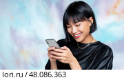 Young Asian Woman with Sleek Bob Scrolling Smartphone with excitement. Молодая женщина азиатского происхождения с гладкой черной стрижкой боб, с увлечением читает на своем смартфоне, на фоне яркого цифрового фона. Стоковое AI-изображение, AI-художник Katsiaryna Repich / Фотобанк Лори