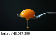 Perfectly cracked egg yolk drips off fork in dark setting. Ярко-желтый яичный желток, удерживаемый вилкой, медленно стекает вниз. Темный фон подчеркивает глянцевую текстуру и цвет желтка, наводя на мысль о кулинарном творчестве. Стоковое AI-изображение, AI-художник Katsiaryna Repich / Фотобанк Лори
