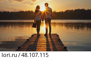 A couple sharing a quiet moment at sunset by the lake, golden light reflecting on the water, their silhouettes creating long shadows. Стоковое AI-видео, аниматор Sergey Grishin / Фотобанк Лори