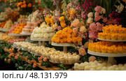 A beautifully arranged assortment of desserts sits on elegant stands, surrounded by lush and colorful flower arrangements, creating a festive atmosphere. Стоковое AI-изображение, AI-художник Данила Большаков / Фотобанк Лори
