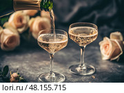 Champagne and red pink roses on a black concrete background. Copy space for text. Valentines drinks for for a pair of lovers. Bartender pours prosecco sparkling wine into glasses. Romance. Wedding Day. Стоковое AI-изображение, AI-художник Марина Демидюк / Фотобанк Лори