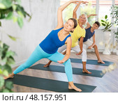 Mom, grandmother and teen grandson performing lateral elongated angle pose Utthita Parshvakonasana. Стоковое фото, фотограф Яков Филимонов / Фотобанк Лори