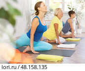 Middle-aged woman practicing pigeon pose of yoga in light fitness room. Стоковое фото, фотограф Яков Филимонов / Фотобанк Лори