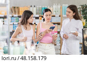 Family of mother and daughter clients choosing box of paracetamol antipyretic pills, scan QR code on label, looking at composition of medicine in drug store, young professional woman pharmacist offering goods and helping with selection. Стоковое фото, фотограф Яков Филимонов / Фотобанк Лори