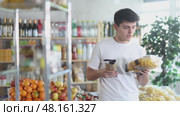 Interested young customer selecting best pasta option for healthy diet, reading label on packages while shopping for groceries in local supermarket. Стоковое видео, видеограф Яков Филимонов / Фотобанк Лори