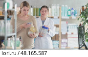 Expecting mother choosing hypoallergenic infant formula at drugstore, using smartphone to check ingredients while smiling caring pharmacist recommending other option for newborns. Стоковое видео, видеограф Яков Филимонов / Фотобанк Лори
