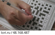 A person actively engages in a crossword puzzle at a cozy cafe. The puzzle grid is partially completed, showcasing various clues and answers. Стоковое видео, видеограф Зворыгина Елена / Фотобанк Лори