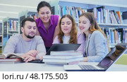 Friendly group of students is preparing for classes on a laptop, studying in the university library. Стоковое видео, видеограф Яков Филимонов / Фотобанк Лори