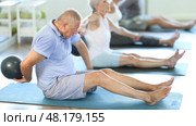 Sitting on floor, mature man with class participants move soft ball around torso. Стоковое видео, видеограф Яков Филимонов / Фотобанк Лори