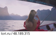 Traveling on lakes, rivers, islands and seas in Asia and Thailand. A young woman in a red dress shoots stunning views Cheow Lan Lake on her phone from a longtail boat, sailing past magnificent cliffs. Стоковое видео, видеограф Владимир Разгуляев / Фотобанк Лори