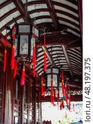 Shanghai, China - 1 April 2025: Traditional Chinese lanterns with red tassels hanging under a curved wooden roof in Yu Garden, a famous historical site in Shanghai. Редакционное фото, фотограф Татьяна Терехина / Фотобанк Лори