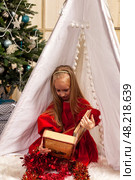 A six-year-old girl model is delightedly discovering the world within a storybook. She sits inside a charming tent surrounded by festive decorations, immersed in her imaginative adventure. Стоковое фото, фотограф Aleksandr Golubev / Фотобанк Лори