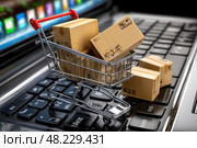Small shopping cart with cardboard boxes on a laptop keyboard. Стоковое AI-изображение, AI-художник Ярославский Максим / Фотобанк Лори