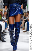 A woman in a blue skirt and boots is walking down a runway. Стоковое AI-изображение, AI-художник Ярославский Максим / Фотобанк Лори