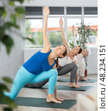 Sporty woman doing standing forward bend Uttanasana, effective yoga pose for back flexibility in group workout. Стоковое фото, фотограф Яков Филимонов / Фотобанк Лори