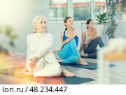 Concentration girl maintaining mental and physical health attending group yoga class at modern studio, practicing twisting poses. Стоковое фото, фотограф Яков Филимонов / Фотобанк Лори