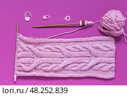 Close-up of accessories for hand knitting on burgundy background. For convenience of knit unusual braid pattern, row counter is put on knitting needle. Pink knitted scarf made of cotton and acrylic yarn. Стоковое фото, фотограф Виктория Катьянова / Фотобанк Лори