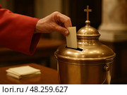 Hand placing ballot in golden chalice at church ceremony. Стоковое AI-изображение, AI-художник Башкирова Анна / Фотобанк Лори