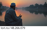 A lone mourner sitting by a river at twilight, his reflection blurred in the water as he whispers prayers for the martyrs of Karba. Стоковое AI-видео, аниматор Sergey Grishin / Фотобанк Лори