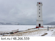 Маяк на заснеженном берегу морской бухты. Побережье Охотского моря. Передний маяк створа бухты Нагаева. Морская бухта покрыта льдом. Вдали виден ледокол и горы. Холодная снежная погода в начале мая на Крайнем Севере России. Парк Маяк, город Магадан, Магаданская область, Россия. Стоковое фото, фотограф Андрей Степанов / Фотобанк Лори