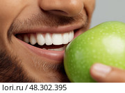 Man Biting into Crisp Green Apple, Natural Dental Health and Fresh Lifestyle Concept. Мужчина кусает хрустящее зеленое яблоко, концепция естественного здоровья зубов и свежего образа жизни. Стоковое AI-изображение, AI-художник Katsiaryna Repich / Фотобанк Лори