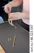 A woman reviewing jewelry, laying out a gold-colored necklace, bracelet, earrings, and ring on a table. Trying on a bracelet. Vertical video. Oblique Angle. Стоковое видео, видеограф Vadzim Yakubovich / Фотобанк Лори
