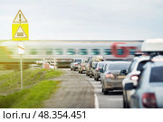 A queue of cars is waiting for a passenger train to travel at a railway crossing outside the city. The automatic barrier prevents unauthorized access to the railway track and ensures trouble-free operation. Стоковое фото, фотограф Владимир Разгуляев / Фотобанк Лори