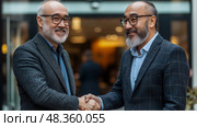 Two men dressed in business attire greet each other with a handshake, showcasing a warm and professional interaction in an urban setting. Стоковое AI-изображение, AI-художник Данила Большаков / Фотобанк Лори