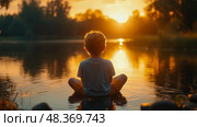 A young boy sits quietly in shallow water, gazing at the sunset reflecting on the lake, surrounded by trees and natural beauty. Стоковое AI-изображение, AI-художник Данила Большаков / Фотобанк Лори