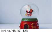 A festive New Year's scene featuring a snow-filled glass ornament with a miniature Santa Claus figurine inside. Gently shaken, the glittering snow swirls around, creating a magical and nostalgic holiday atmosphere. Стоковое видео, видеограф Алексей Круковский / Фотобанк Лори