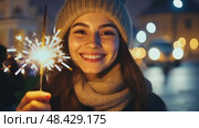 Smiling Girl with Fire Sparkler Glow in the Winter Season. pleased happy smiling young 20s woman is holding a bright sparkler in a festive winter setting. Glowing blur bokeh light on background. Стоковое AI-видео, аниматор Марина Демидюк / Фотобанк Лори