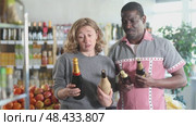 African man with European wife hold bottle and choose alcohol, wine or beer bottle in store. Стоковое видео, видеограф Яков Филимонов / Фотобанк Лори