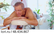 Relaxed old man undergoing back massage therapy conducted by skilled masseuse in light room. Стоковое видео, видеограф Яков Филимонов / Фотобанк Лори