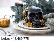 A mysterious black skull with golden roses and pumpkins on serving plates for a Halloween or Day of the Dead party. Стоковое фото, фотограф Photojuli / Фотобанк Лори