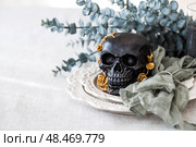 A mysterious black skull with golden roses and pumpkins on serving plates for a Halloween or Day of the Dead party. Стоковое фото, фотограф Photojuli / Фотобанк Лори
