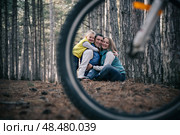 A family rides bicycles through the forest. A creative perspective through a bicycle wheel. Стоковое фото, фотограф София Тюленева / Фотобанк Лори