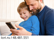Father and son little boy laughing and using phone. They watching funny videos together, playing games on smartphone. Concept technology, smart phone addicted. Fun weekend activity. Modern fatherhood. Стоковое фото, фотограф Марина Демидюк / Фотобанк Лори