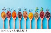 Culinary art: Wooden Spoons Filled with Variety of Aromatic Spices on a Blue field, A flavour enhancer. Стоковое AI-изображение, AI-художник Данила Большаков / Фотобанк Лори