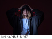 A teenage girl in a black hoodie with a hood on a black background. Holds his head with his hands. The concept of problems in adolescents and the difficulties of the transition period. Стоковое фото, фотограф Луиза Налимова / Фотобанк Лори