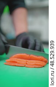 Professional chef in black gloves carefully slicing fresh salmon fillet into thin sashimi pieces on green cutting board for gourmet seafood preparation. Стоковое видео, видеограф Данил Руденко / Фотобанк Лори