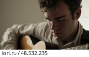 A man with curly hair playing a guitar, strumming chords with his fingers and creating music with passion and skill. Стоковое AI-изображение, AI-художник Данила Большаков / Фотобанк Лори
