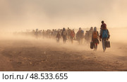 Migrants journey through desert landscape at dusk. Стоковое AI-изображение, AI-художник Olga Didraga / Фотобанк Лори